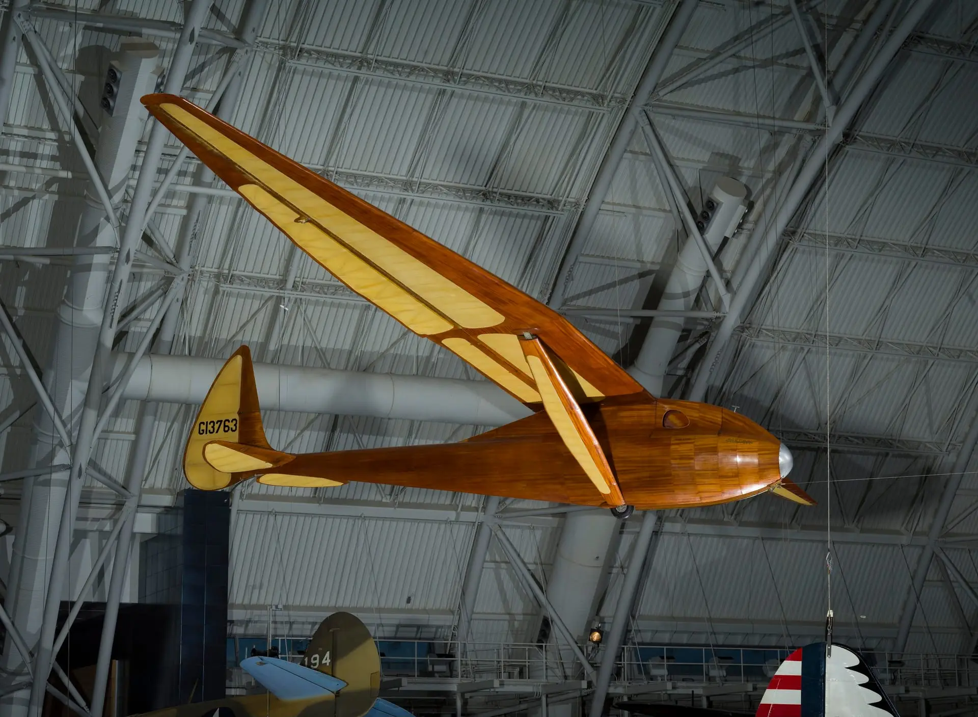 A wooden 1930s glider hanging from the roof of a hangar